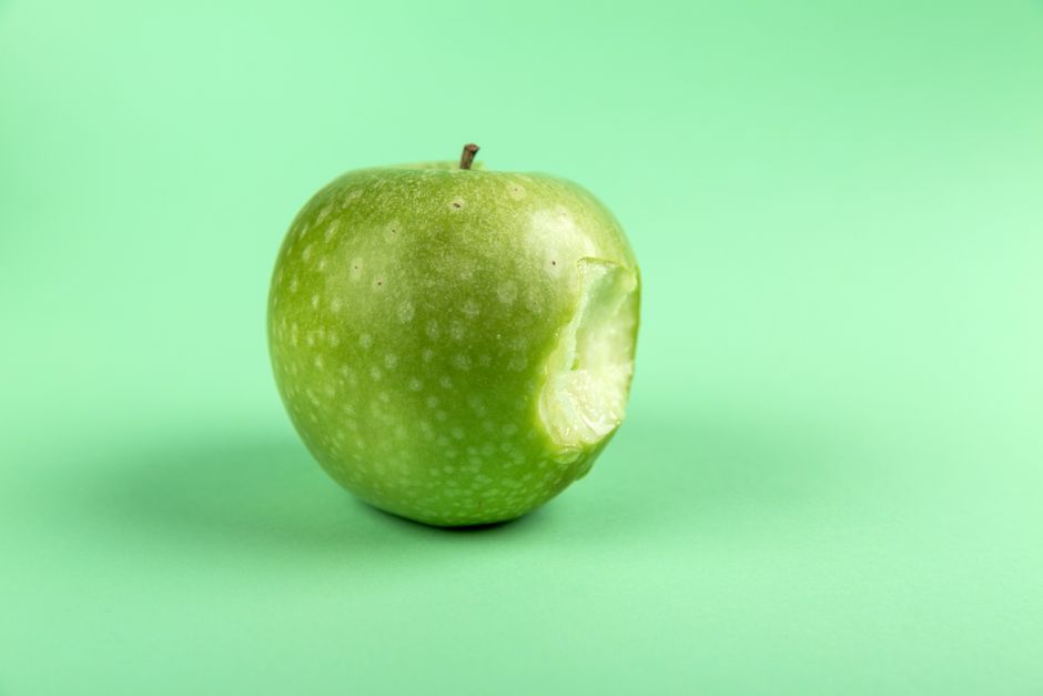 Una manzana verde fresca y mordida sobre una superficie verde simple. Perfecta para diseños de salud y comida.