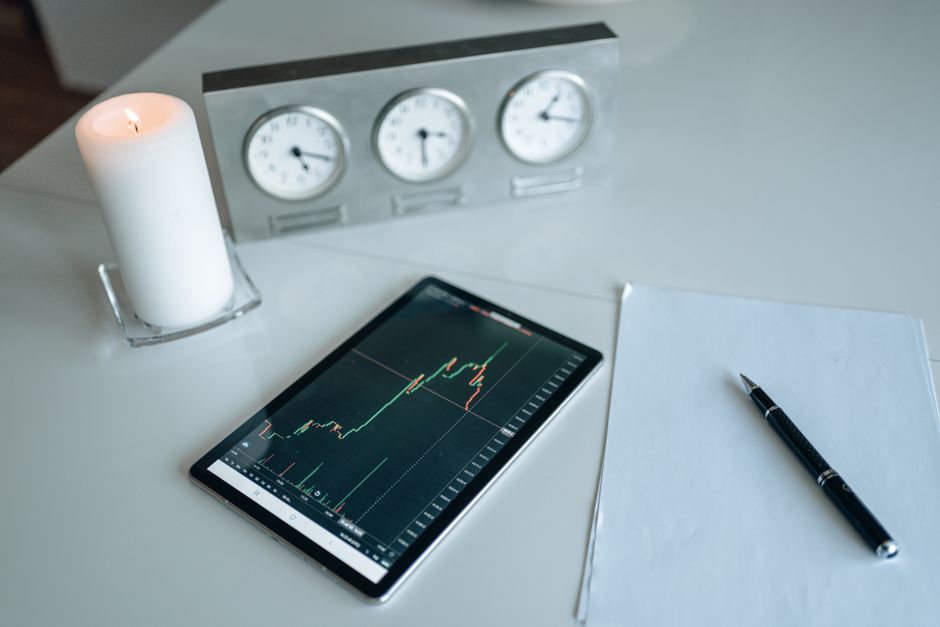 Tableta mostrando gráfico de trading junto a vela y papeles en un entorno de oficina.