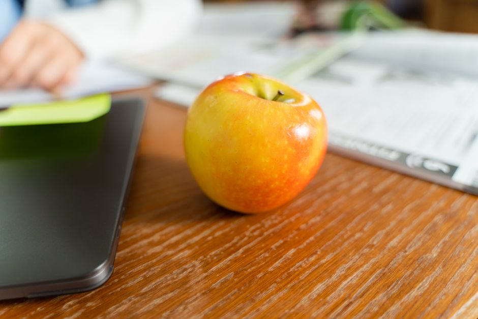 Una manzana madura se encuentra sobre un escritorio de madera junto a un portátil, transmitiendo un ambiente de trabajo saludable.
