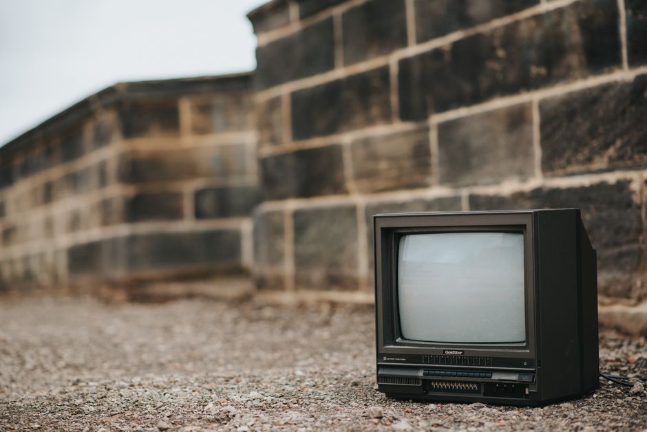 Un televisor vintage abandonado colocado en la acera junto a una pared de ladrillos, evocando nostalgia.