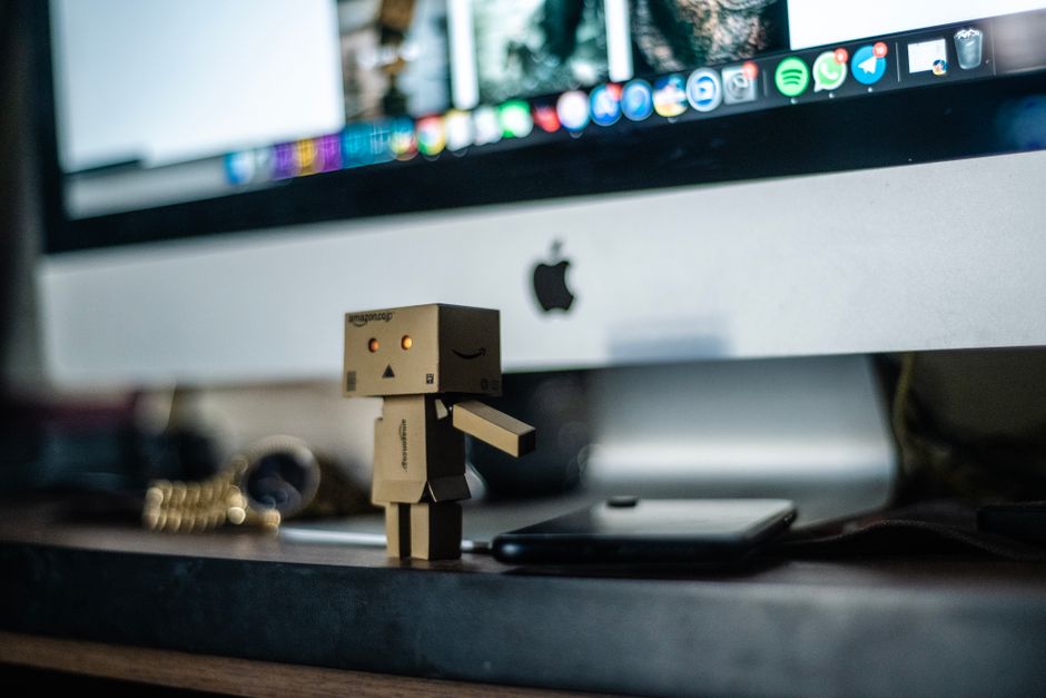 Un pequeño juguete robot de cartón expuesto frente a una pantalla de ordenador, añadiendo encanto al espacio de trabajo.