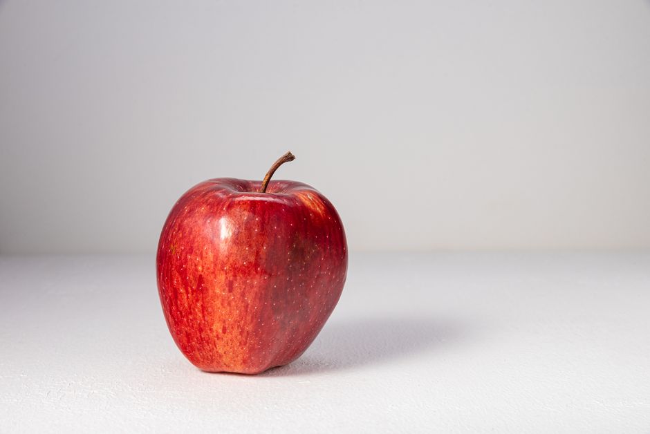 Primer plano de una manzana roja fresca sobre una superficie blanca, destacando su piel brillante.