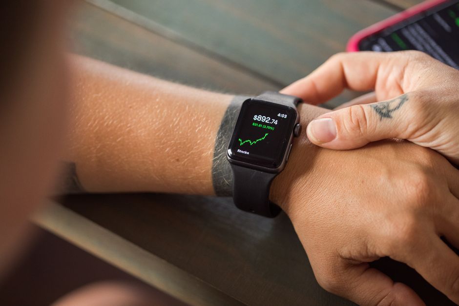 Primer plano de un reloj inteligente mostrando datos del mercado de valores, con manos que lo llevan puesto.