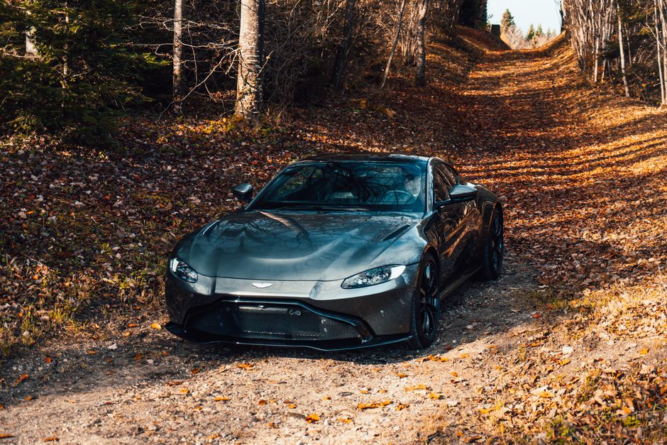Un impresionante automóvil deportivo Aston Martin estacionado en un pintoresco sendero natural cubierto de otoño.