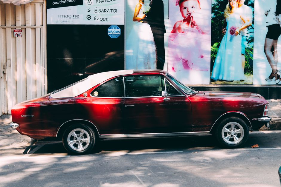 Coche antiguo rojo aparcado en una calle urbana con carteles publicitarios.