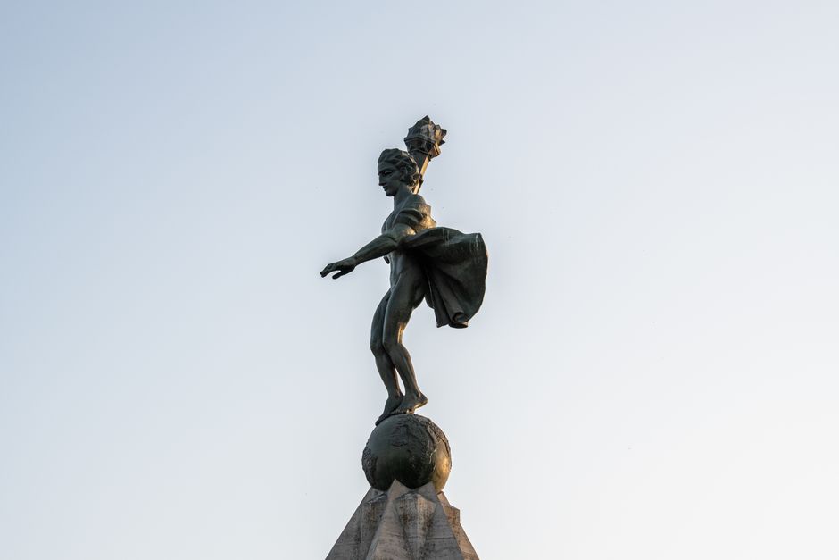 Una impactante estatua de Atlas en una pose dinámica, capturada bajo un cielo claro de la tarde.