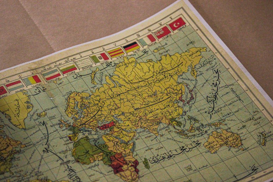 Antiguo mapa mundial que muestra continentes, escritura árabe y varias banderas nacionales.