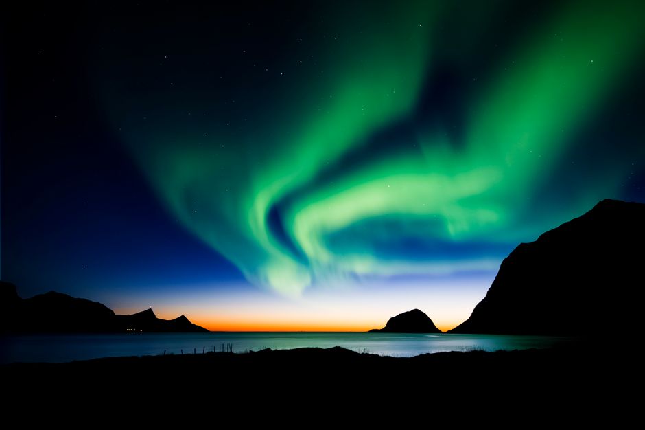 Impresionante vista de las Luces del Norte bailando sobre las montañas y el mar en Lofoten, Noruega, por la noche.