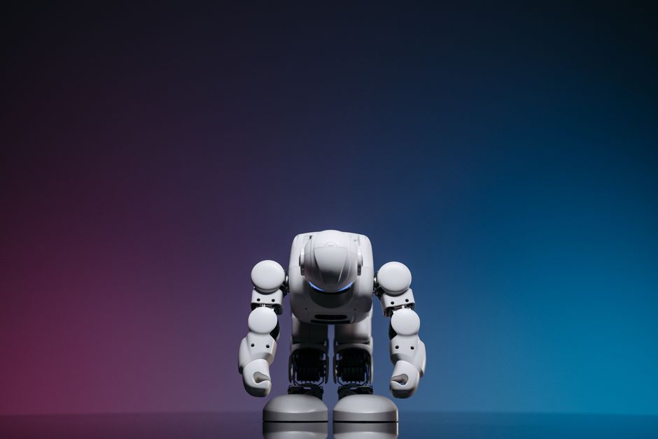 Robot blanco en pose de reverencia contra un fondo de estudio en degradado.