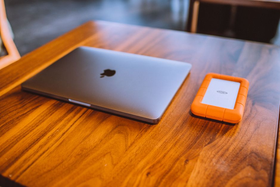 Un portátil elegante y un disco duro externo resistente sobre una mesa de madera con estilo en un interior.