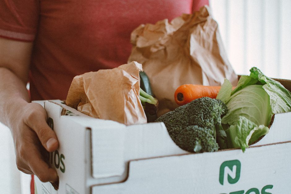 Persona sosteniendo una caja llena de verduras frescas, ideal para conceptos de salud y productos.