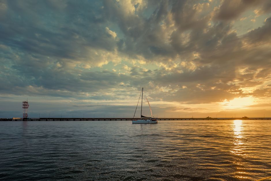 Una escena tranquila de un velero en aguas calmadas bajo un dramático cielo al atardecer.