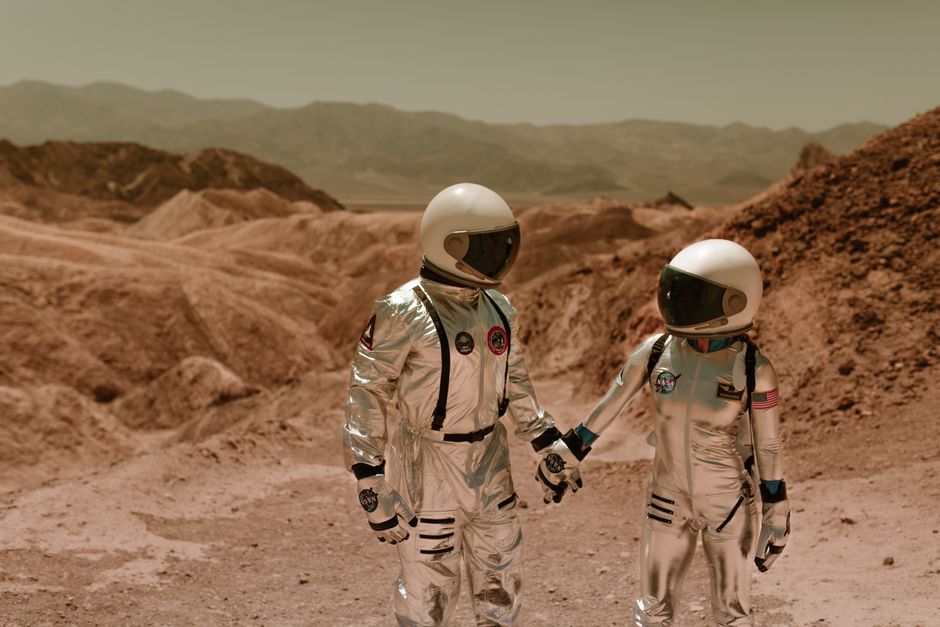 Dos astronautas con trajes espaciales explorando un paisaje árido de ciencia ficción.
