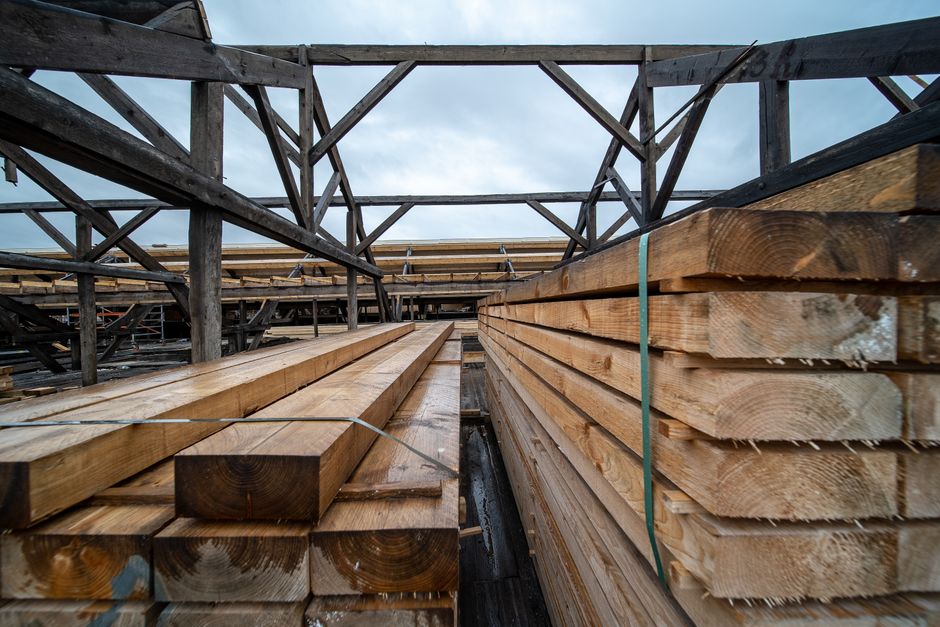 Tablones de madera apilados en un área de almacenamiento industrial al aire libre bajo un cielo nublado.