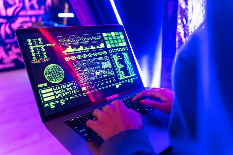 Persona escribiendo en un portátil con una vibrante pantalla de datos digitales, destacando la ciberseguridad.