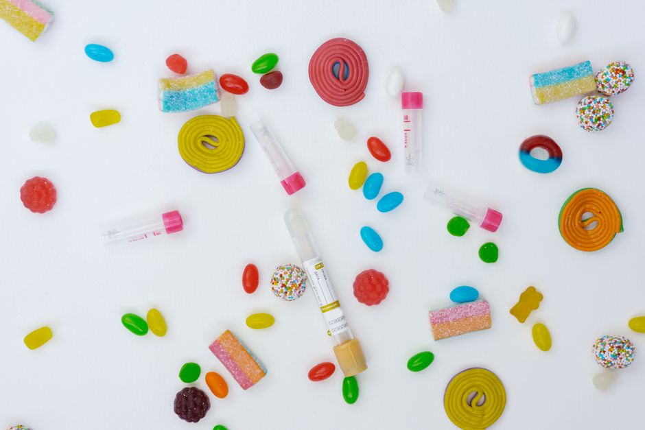 Dulces dispersos y lápices de insulina sobre una superficie blanca, vibrantes y conceptuales.