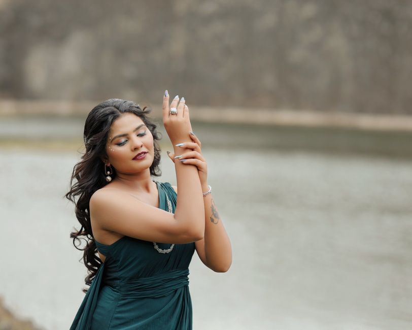 Una elegante mujer con un vestido verde posa con gracia a la orilla del río, luciendo joyas.
