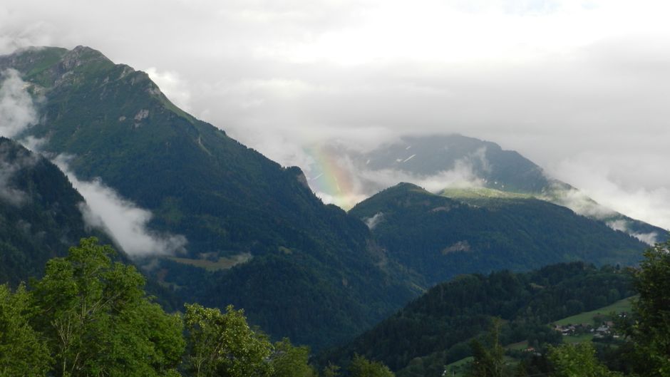 Impresionante vista de las montañas suizas con un arcoíris entre las nubes, capturando la belleza natural.