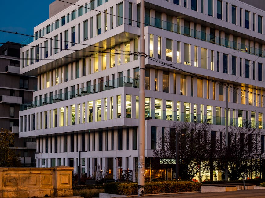Un moderno edificio de oficinas con interior iluminado, fotografiado al atardecer.