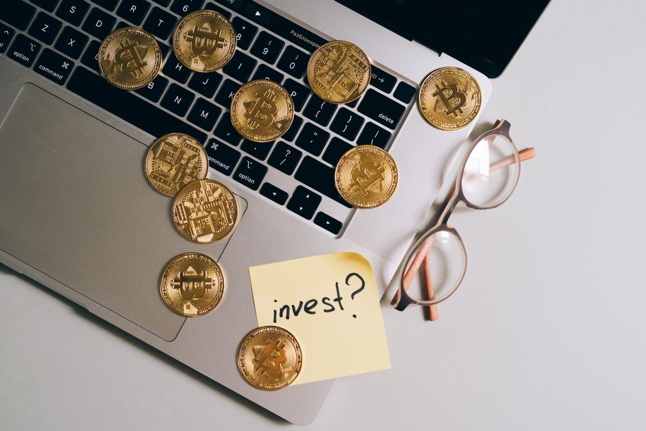 Portátil con monedas de Bitcoin, gafas y nota '¿invertir?'. Ideal para temas de finanzas y tecnología.
