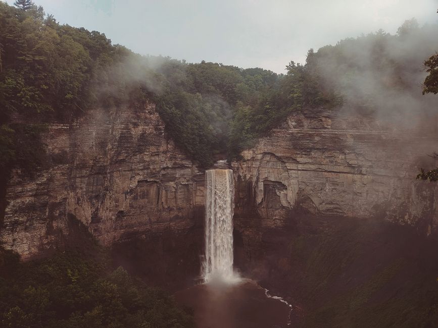 Majestuosa cascada cayendo por un desfiladero rocoso envuelto en niebla y exuberante vegetación.