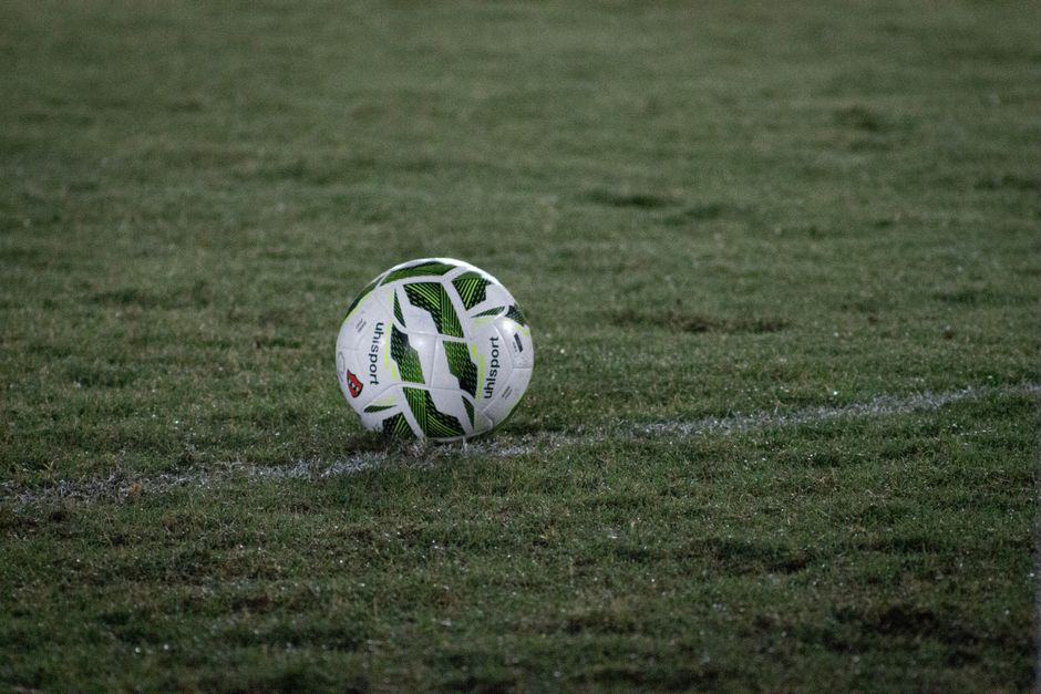 Un balón de fútbol sobre un campo de hierba, fotografiado al anochecer con el rocío visible.