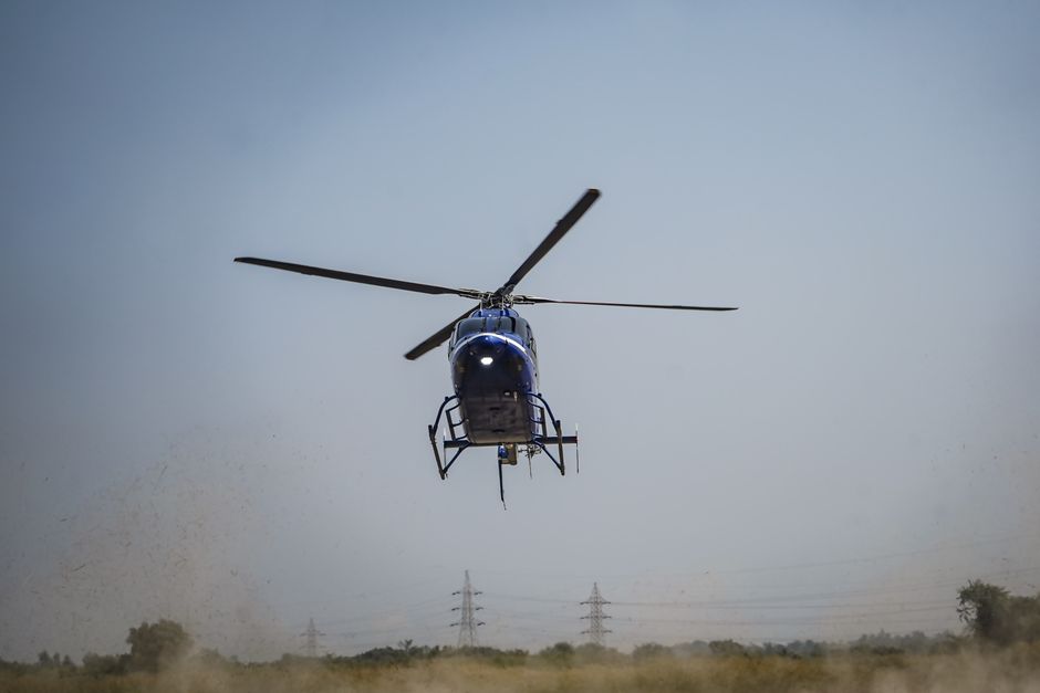 Un helicóptero azul despega, levantando polvo en un entorno al aire libre.