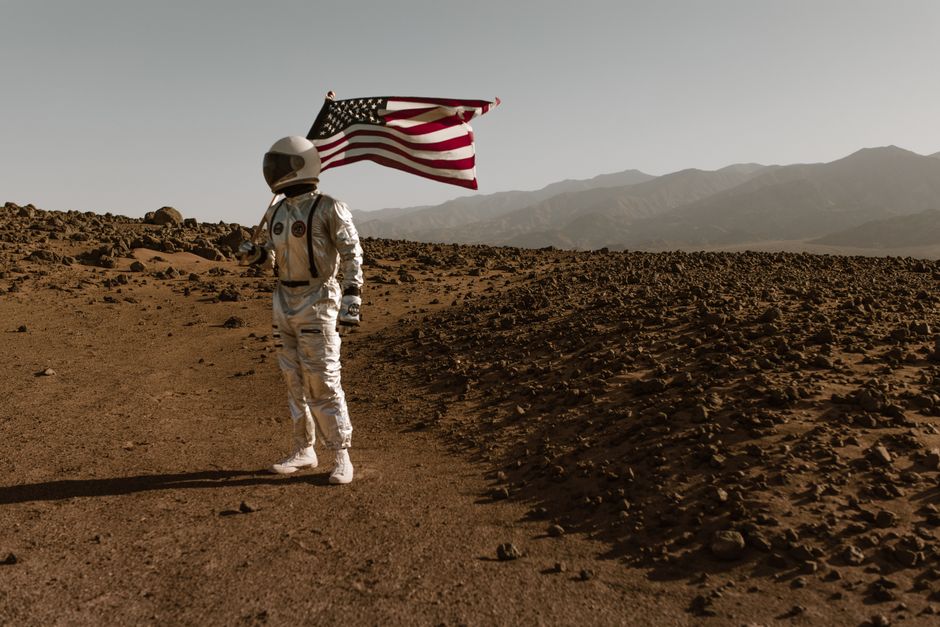 Astronauta de pie en un paisaje árido sosteniendo la bandera americana. Imagen conceptual de exploración espacial.