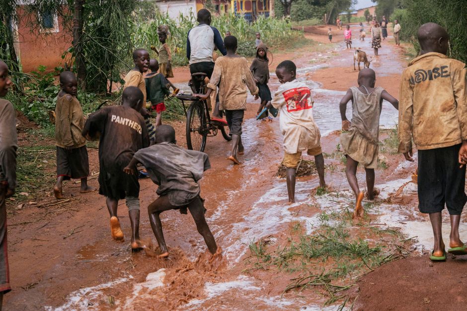 Un grupo de niños juega alegremente en un sendero embarrado en un pueblo rural, creando una escena animada.