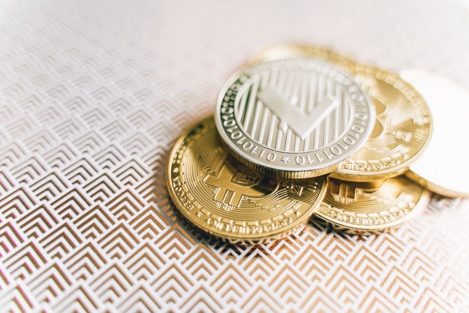 Pila de monedas de Bitcoin y Litecoin sobre una superficie texturizada geométrica, simbolizando finanzas digitales.