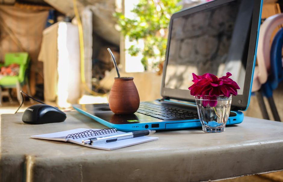Un tranquilo espacio de trabajo al aire libre con un portátil, cuaderno, taza y flores en una mesa.