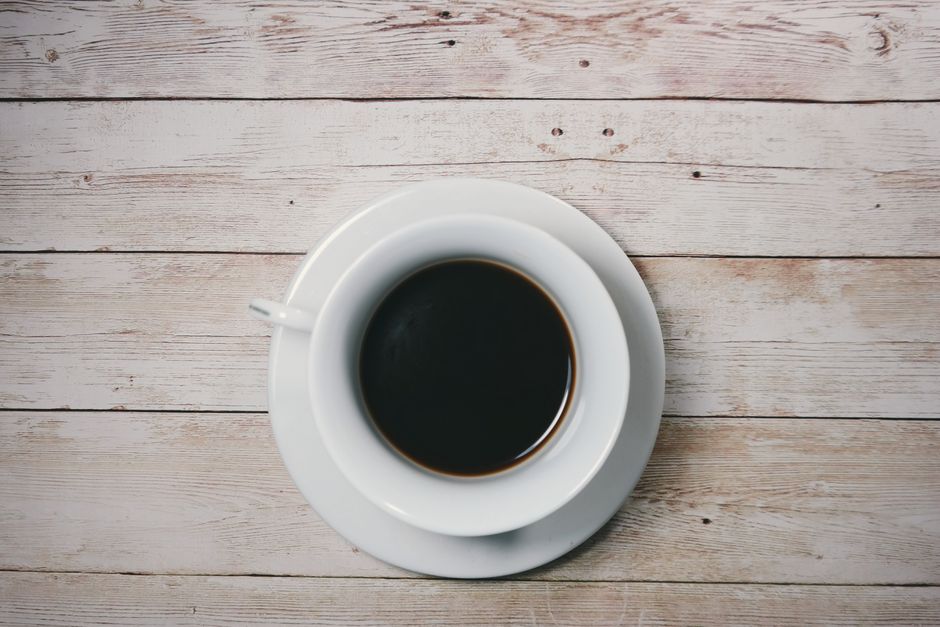 Una taza de café negro sobre una mesa de madera rústica, capturada desde arriba.