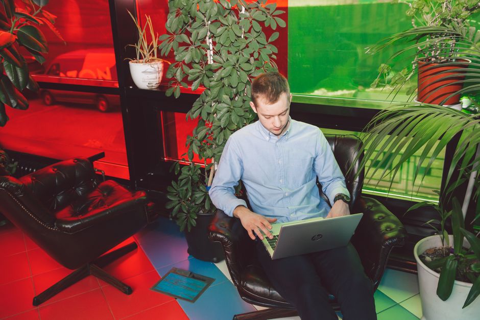 Joven hombre usando laptop en un entorno moderno vibrante y lleno de plantas para trabajo remoto.