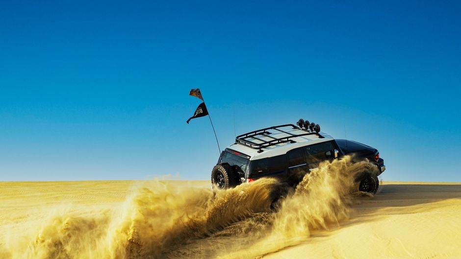 Poderoso SUV conduciendo a través de las dunas de arena del desierto bajo un cielo azul claro.