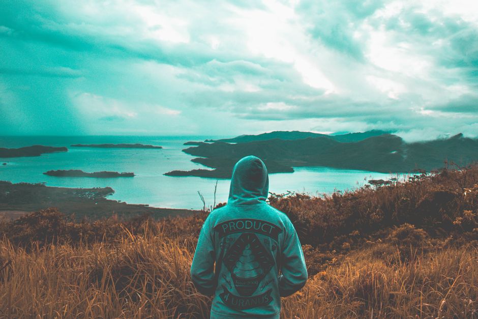 Persona con sudadera contemplando una hermosa vista costera con islas bajo un cielo nublado.