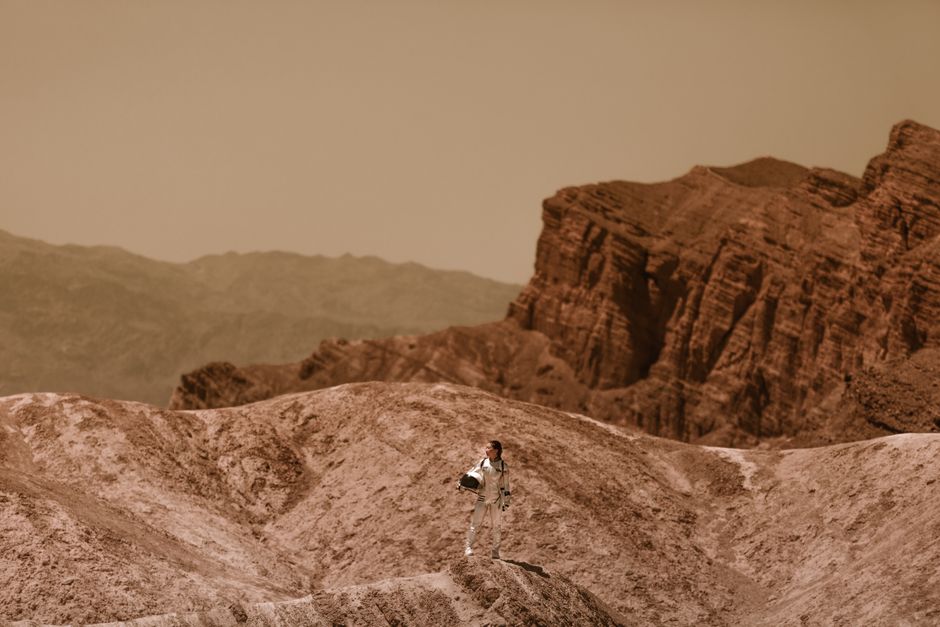 Una mujer astronauta se encuentra en un terreno árido y alienígena, simbolizando la colonización del espacio.
