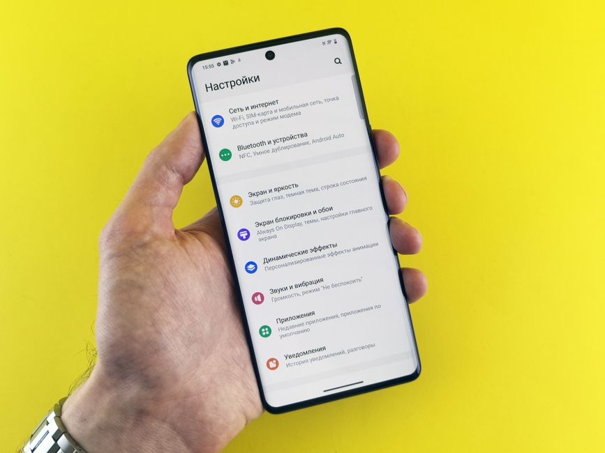 Primer plano de una mano que sostiene un teléfono inteligente con un menú de configuración sobre un fondo amarillo brillante.