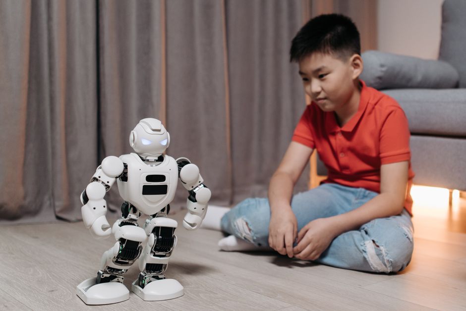 Un niño asiático sentado en el suelo, interactuando con un robot blanco, mostrando innovación y tecnología.