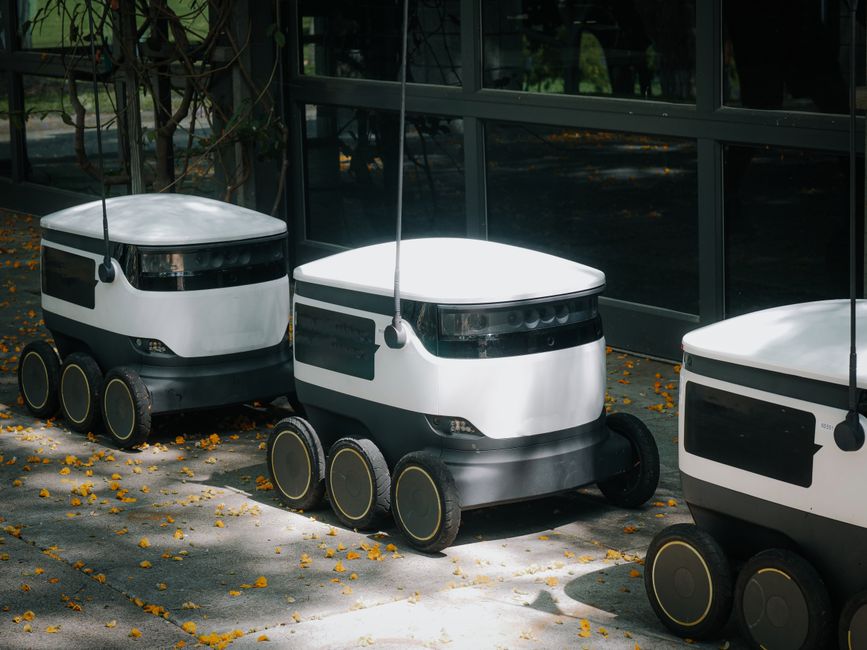 Robots de entrega autónomos en una acera durante el día, mostrando tecnología moderna.