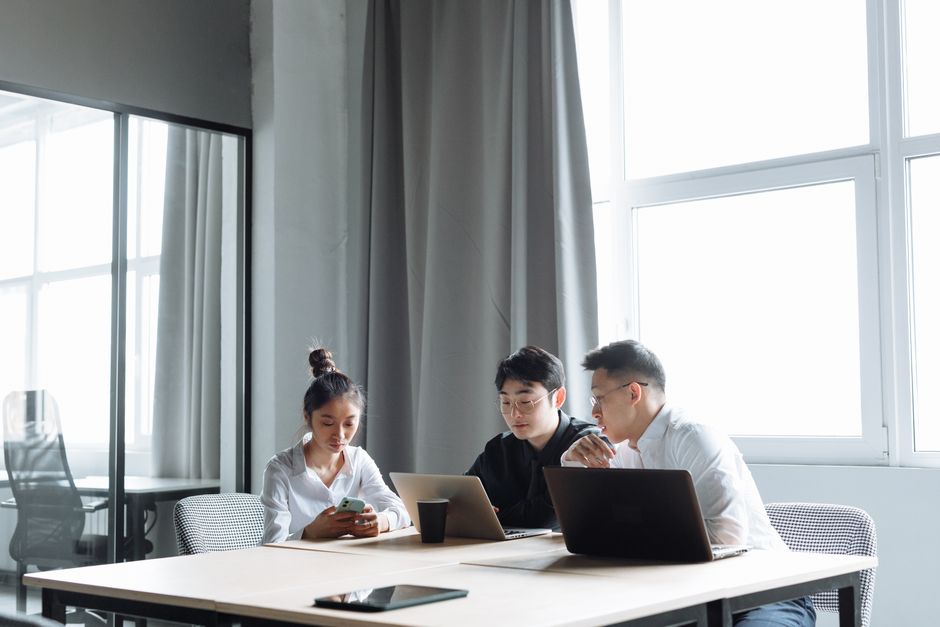 Tres profesionales colaboran en laptops en un entorno de oficina moderno y luminoso.