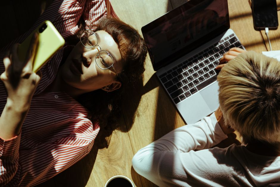 Dos adultos relajándose con smartphone y laptop en un ambiente interior acogedor.