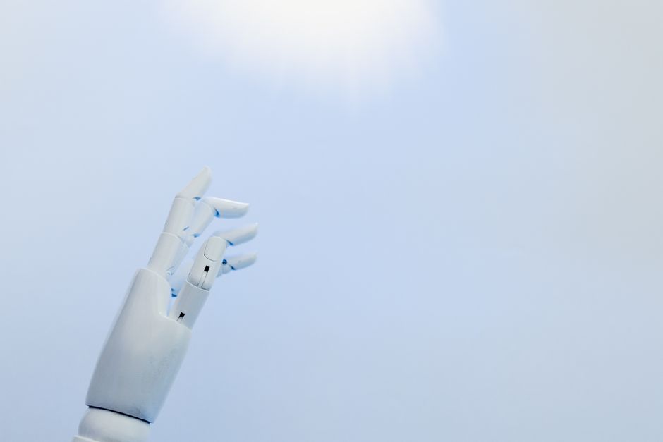 Una mano robótica alcanzando hacia una luz brillante sobre un fondo blanco simbolizando innovación.