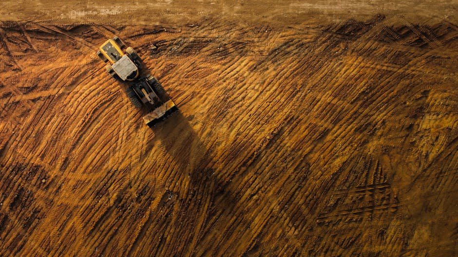 Vista de arriba hacia abajo de una excavadora moviendo tierra en un gran sitio de construcción.