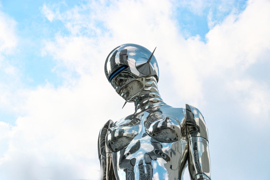 Una escultura de robot cromado elegante se encuentra contra un fondo de cielo azul brillante.