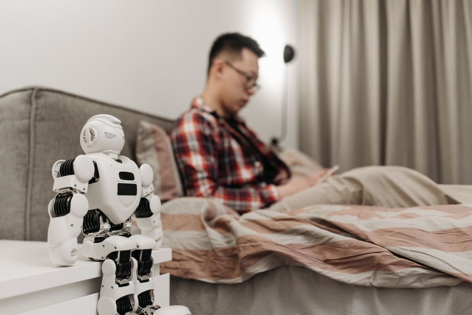 Un dormitorio moderno con un robot en la mesa de noche y un hombre sentado en la cama.