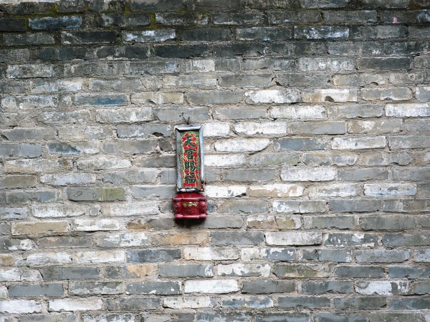 Un letrero chino tradicional colgado en una antigua pared de ladrillo texturizado, transmitiendo herencia cultural e historia.
