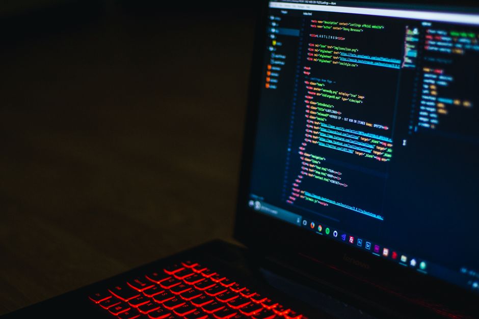 El teclado retroiluminado en rojo y el código en la pantalla del ordenador portátil crean un ambiente tecnológico.