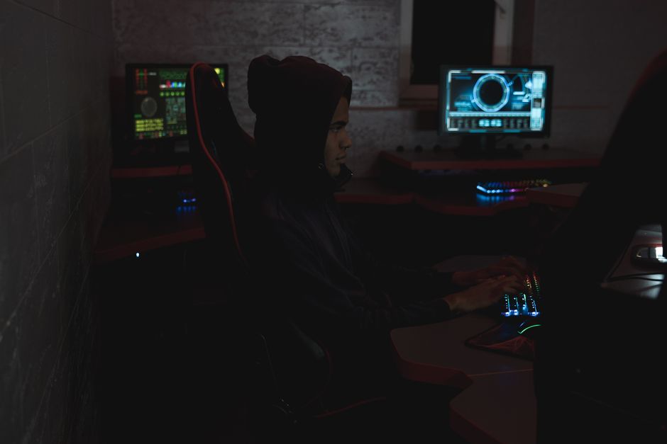 Un profesional analizando datos en múltiples monitores en una sala oscura, resaltando temas de ciberseguridad.