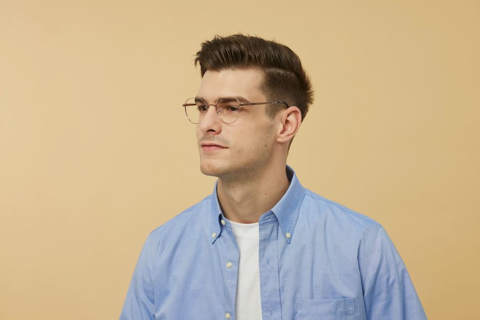 Retrato de un joven con gafas y una camisa azul, luciendo serio contra un fondo neutro.