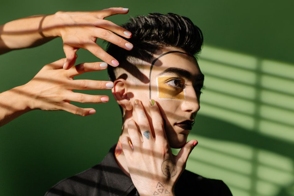 Retrato artístico de una persona con maquillaje creativo y juego de sombras sobre un fondo verde.